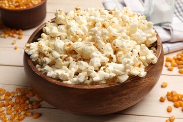 Tasty popcorn and corn kernels on light wooden table, closeup