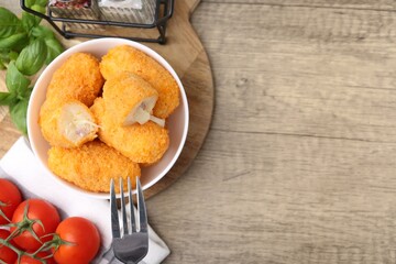 Delicious fried croquettes in bowl, tomatoes and spices on wooden table, flat lay. Space for text