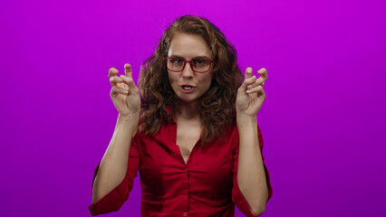 Woman in red shirt wearing glasses gestures quotation marks with fingers against vibrant pink background, expressing sarcasm or irony with focused expression.