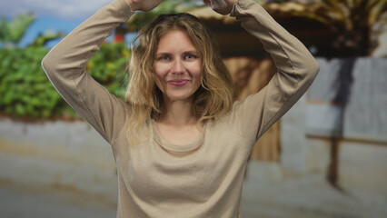 Woman with arms raising poses at a beach backdrop featuring a blonde young smiling subject...