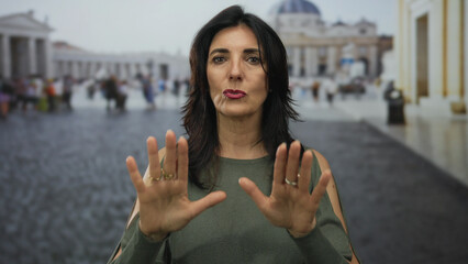 Woman in green top holds hands forward in open palm gesture before historic building facade at...