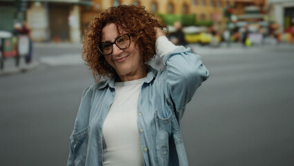 Fototapeta premium Woman smiling on a busy city street with blurred background, wearing glasses and casual attire, exuding joyful confidence in an urban outdoor setting.
