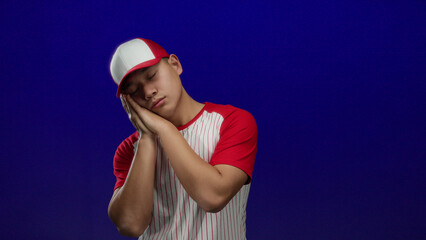 Young chinese man in baseball uniform with red and white stripes posing sleepily against isolated...