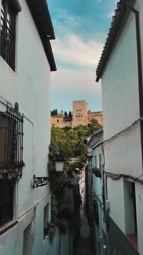 Cinematic alley view in Granada revealing Alhambra fortress between whitewashed houses