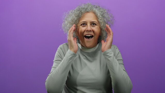 Middle-aged woman with grey hair against a purple background expressing surprise in casual attire.