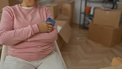 Woman resting in a new home surrounded by moving boxes holding a smartphone in a cozy living room.