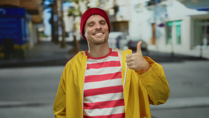 Young man in a yellow jacket gives thumbs up on a city street, showcasing a positive attitude and...