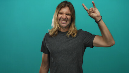 Blond man with long hair and bare arms grins and shows rock horns gesture in studio; rock fun...