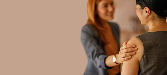 Businesswoman in office with hand on colleague shoulder offering support and encouragement during work