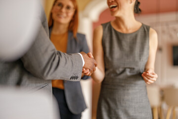 Midsection of businessman greeting cheerful female coworker with handshake in meeting at corporate office
