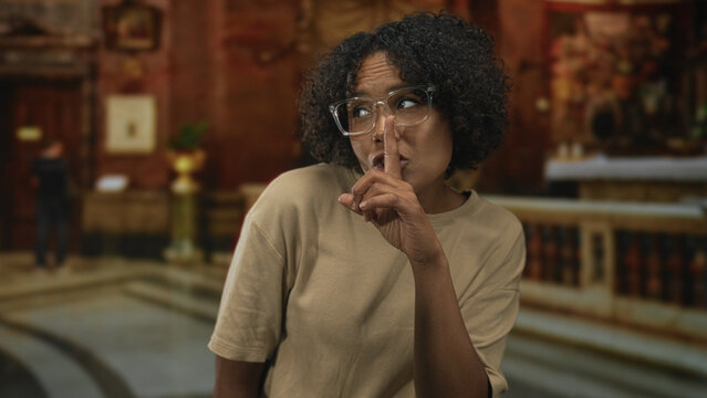 Woman holds finger to lips for silence inside ornate church building interior with carved wooden altar in view; reverence reflection.