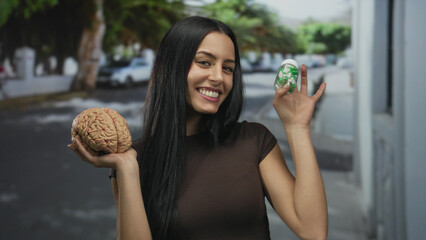 Woman smiling happily on a city street holding a model brain and bottle of pills, showcasing a...