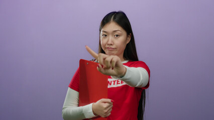 Woman pointing with a serious expression in a red volunteer shirt holding a clipboard against a...