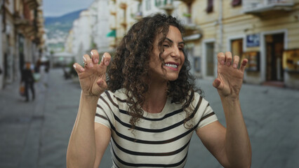 Woman with open mouth and raised hands making a roaring gesture on an urban city street lined with...