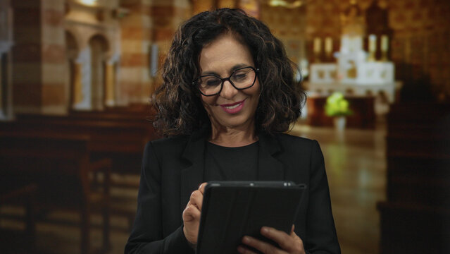 Woman with glasses using tablet in a beautifully lit church setting, highlighting her middle-aged hispanic heritage with a peaceful interior backdrop.