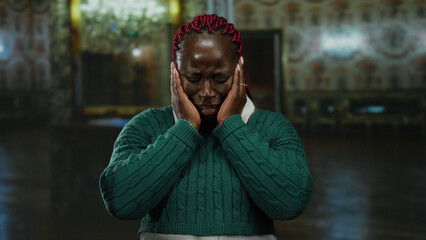 Woman in green sweater crying indoors at museum with chandelier and ornate decor background evoking...