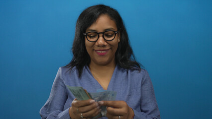 Woman counting malaysian ringgit banknotes in blue studio with glasses and smiling while sorting...