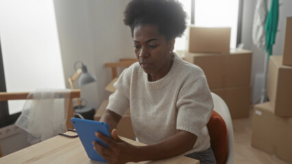 Woman using tablet in new apartment surrounded by boxes suggests moving and modern technology in...