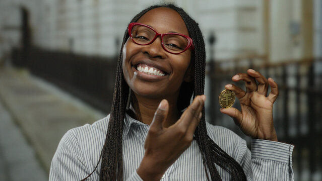 Woman smiles holding crypto coin on urban street emphasizing virtual currency and blockchain in a city setting.