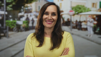 Fototapeta premium Young hispanic woman crosses arms with slight smile and closed eyes on sunlit street; denial rejection.