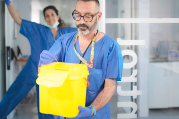 Doctor disposing of needle in sharps container in hospital