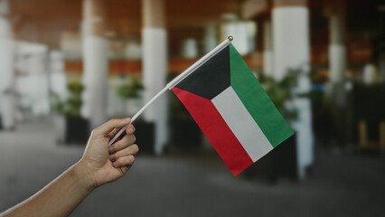 Male hand holding kuwait flag in vibrant outdoor city setting displaying national pride and...