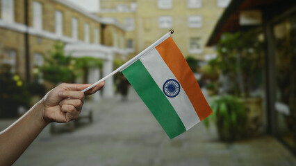 Hand holding indian flag outdoors in city street scene, symbolizing nationalism and pride in urban...