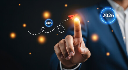 Naklejka premium Businessman using his finger to guide a paper plane from a circle with the year 2025 to a glowing circle with the year 2026, representing future business strategy and growth