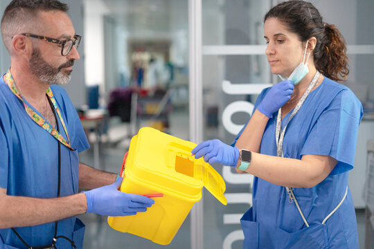 Two healthcare professionals handling a sharps disposal container in hospital setting