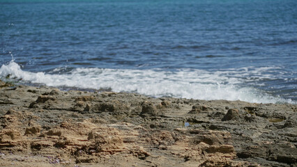 Mediterranean coastline with rocky shore and gentle waves under a clear sunny sky, capturing the beauty and tranquility of the seaside landscape.