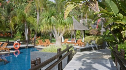 Blurred view of a luxurious tropical resort with defocused palm trees, outdoor pool, and sun loungers, offering a serene, bokeh-filled ambiance ideal for relaxation.