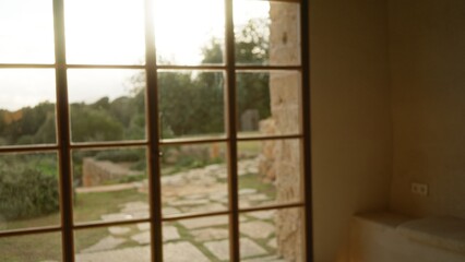 Indoor view through a large glass window showcasing a blurred, picturesque mediterranean garden...