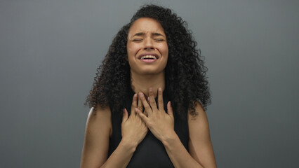 Woman expressing distress over isolated grey background, hands touching face, youthful, hispanic,...