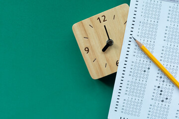 close up pencil and answer sheets on the clock with green background, education concept