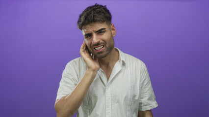 Young hispanic man touches ear with right hand and grimaces in studio; discomfort uncertainty...