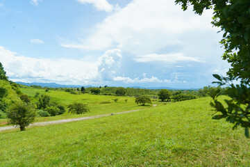 Scenic view of the Plain of Jars archaeological site in Xieng Khouang, Laos. The landscape features ancient megalithic stone jars scattered across a lush green meadow, with rolling hills, distant moun