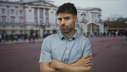 Man with crossed arms and bare forearm standing on a crowded city street in front of a palace...