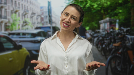 Woman wearing a white shirt gestures with open palms revealing bare hands amidst city traffic on street; openness sincerity.