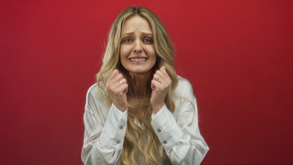 Woman expressing emotions in front of a vivid red wall; young blonde with hands clasped in appeal...