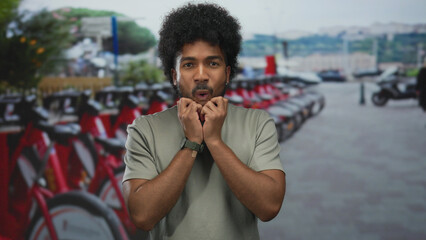 Excited african american man at outdoor bike rental with red bicycles in background, expressing joy amid bustling urban scene.