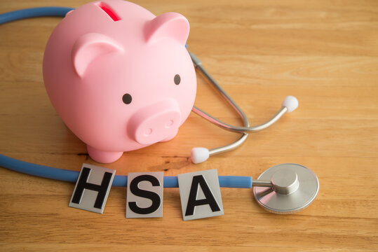 HSA alphabet, pink piggy bank and stethoscope on wooden table background. Health savings account (HSA), money management for medical treatment, health and life insurance, wellbeing and so on concept.