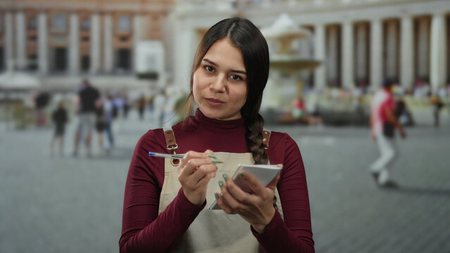 Hispanic waitress wearing apron takes notes outside in vatican city's san pedro square amid tourists and iconic architecture.