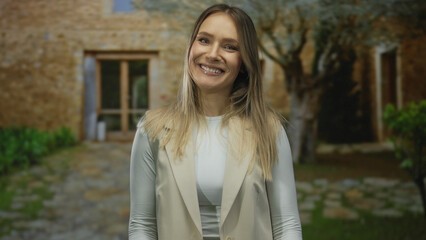 Fototapeta premium Woman smiling and pointing at camera on a city street with stone buildings in daylight.