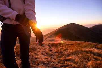 Hiker putting on gloves during sunset hike in the mountains. Close-up of traveler on scenic trail with warm golden light