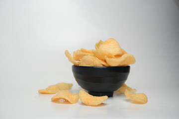 Traditional Indonesian kerupuk crackers served in a black bowl, with pieces scattered on a white surface, showcasing their crunchy texture.

