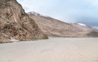 Peaceful Yarab Tso lake in Nubra Valley, Ladakh with white sandy shore, Himalayan mountains, and dramatic cloudy sky. Scenic nature, travel, and meditation background.