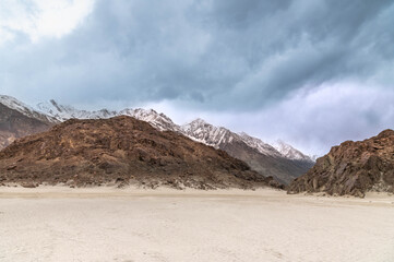 Peaceful Yarab Tso lake in Nubra Valley, Ladakh with white sandy shore, Himalayan mountains, and dramatic cloudy sky. Scenic nature, travel, and meditation background.