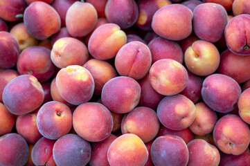 Fresh peaches are piled together in a wooden crate at an outdoor market,