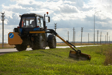 Mowing grass along the highway. Tractor with mounted edge mower at work.