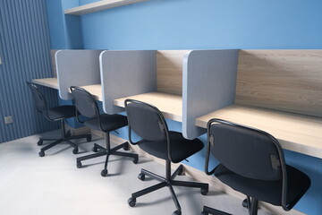 Minimalist study area featuring individual cubicles, ergonomic office chairs, blue walls, and light wood desks in a clean workspace.
